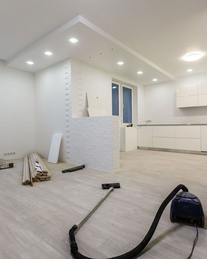 Interior during renovation; white walls, ceiling with recessed lighting, light wood floors, vacuum cleaner.