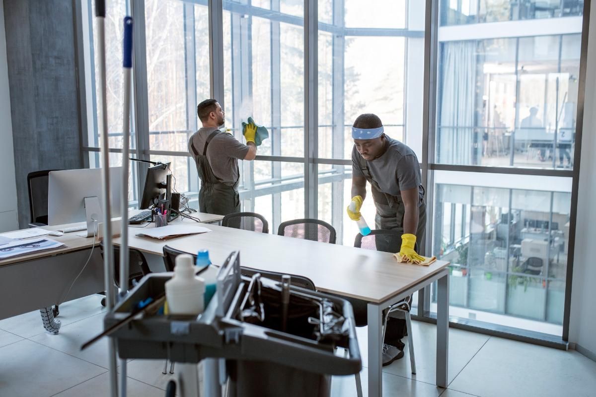 Everyday Clean Services office cleaning with staff wiping windows and cleaning a desk wearing yellow gloves.
