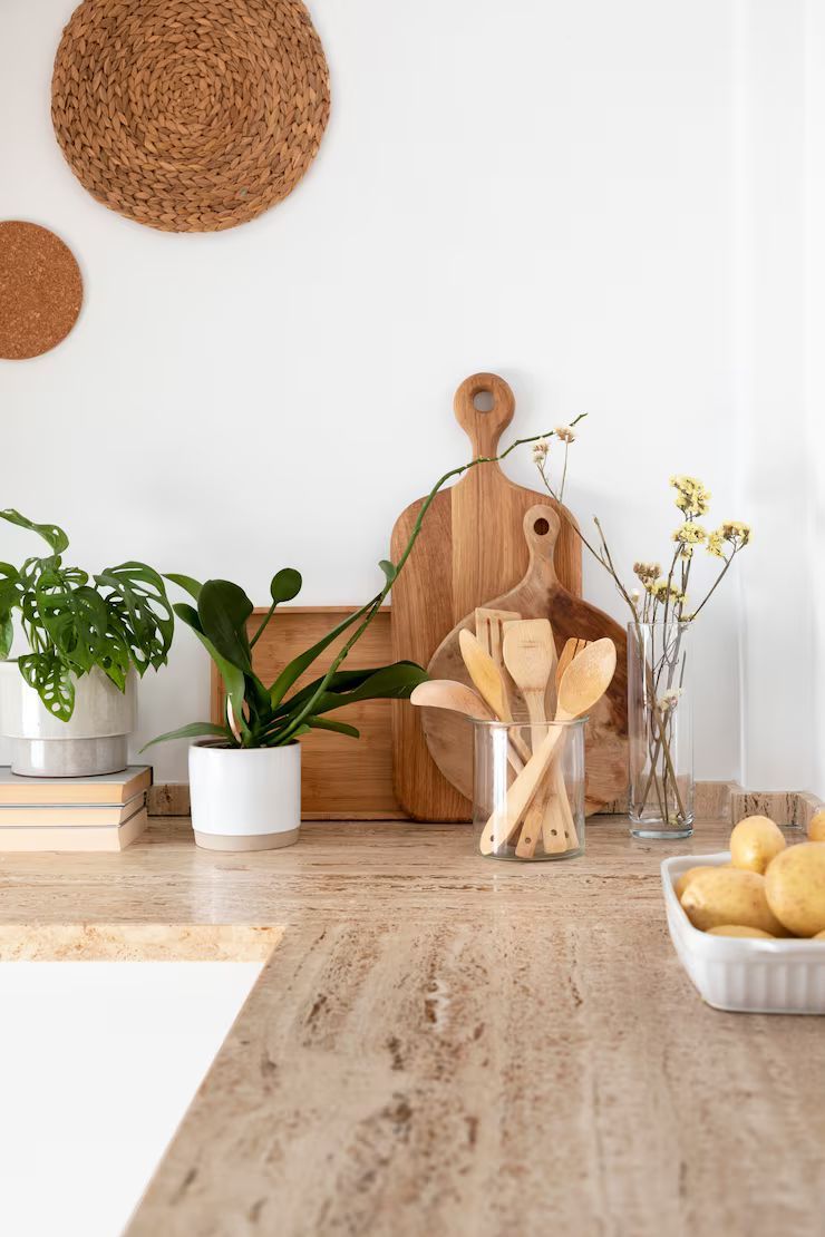 Kitchen countertop with wooden cutting boards, utensils, plants, and potatoes.