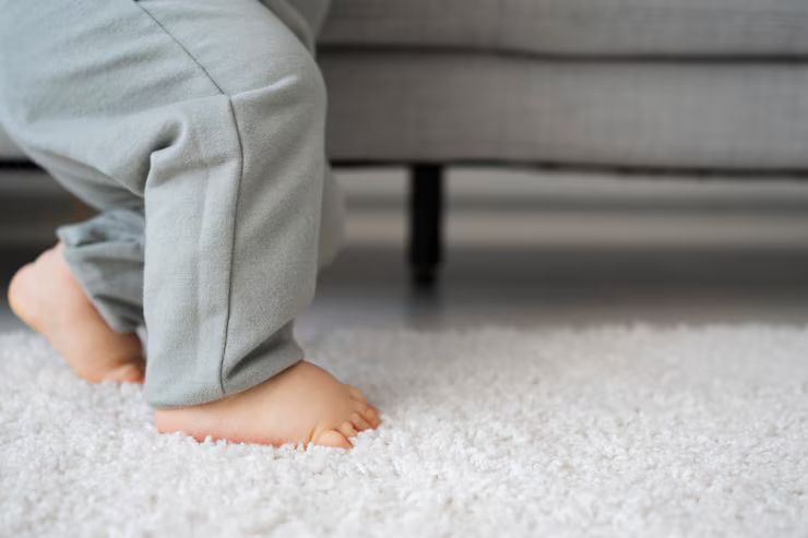 Bare feet on a white rug, legs in gray pants near a gray couch.
