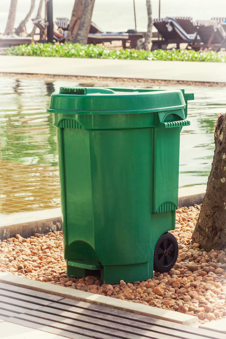 Green trash bin with wheels by a pool.