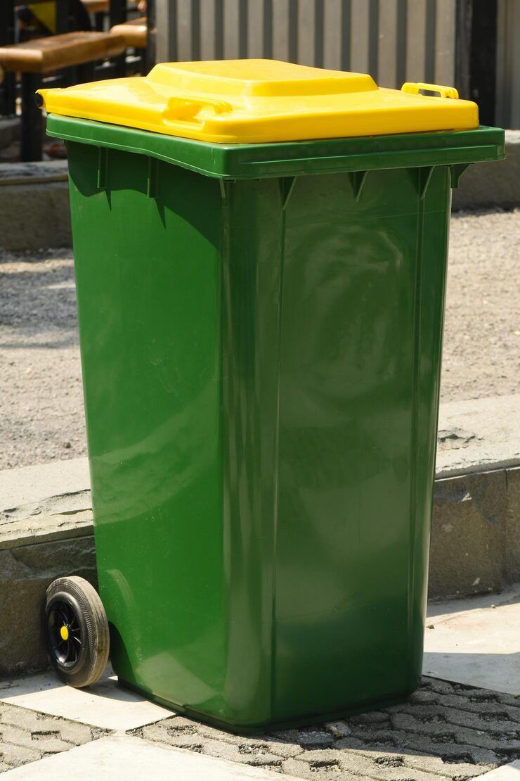 Green and yellow trash bin with wheels on a sidewalk.