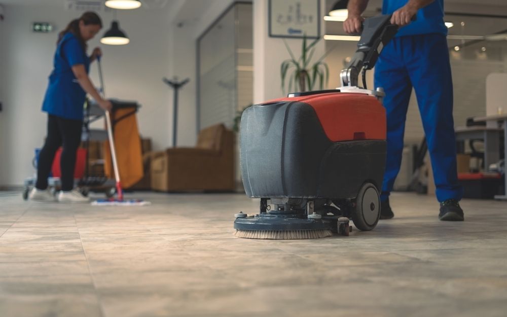 Floor cleaner machine in use with another cleaning person mopping in the background.