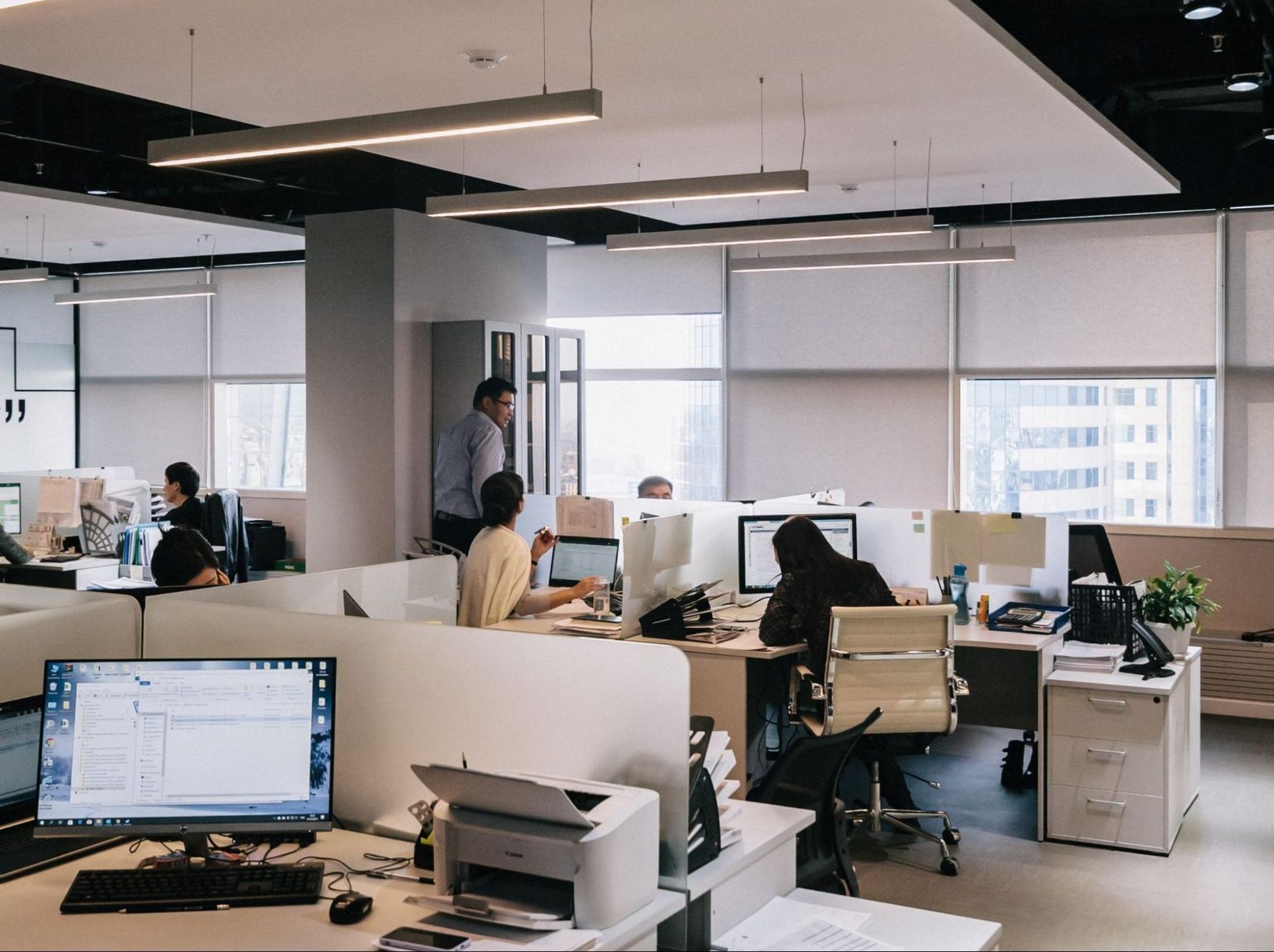 Office interior with people at workstations, working on computers. Modern design, natural light.
