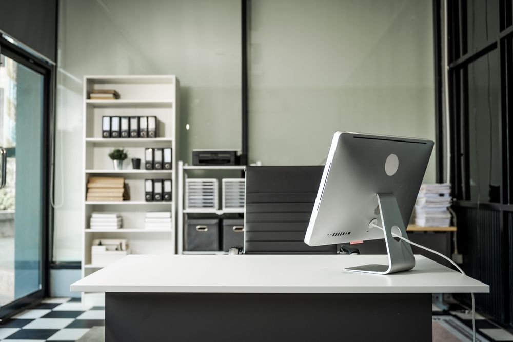 Modern office with a white desk, computer monitor, and shelving unit. Black and white checkered floor.