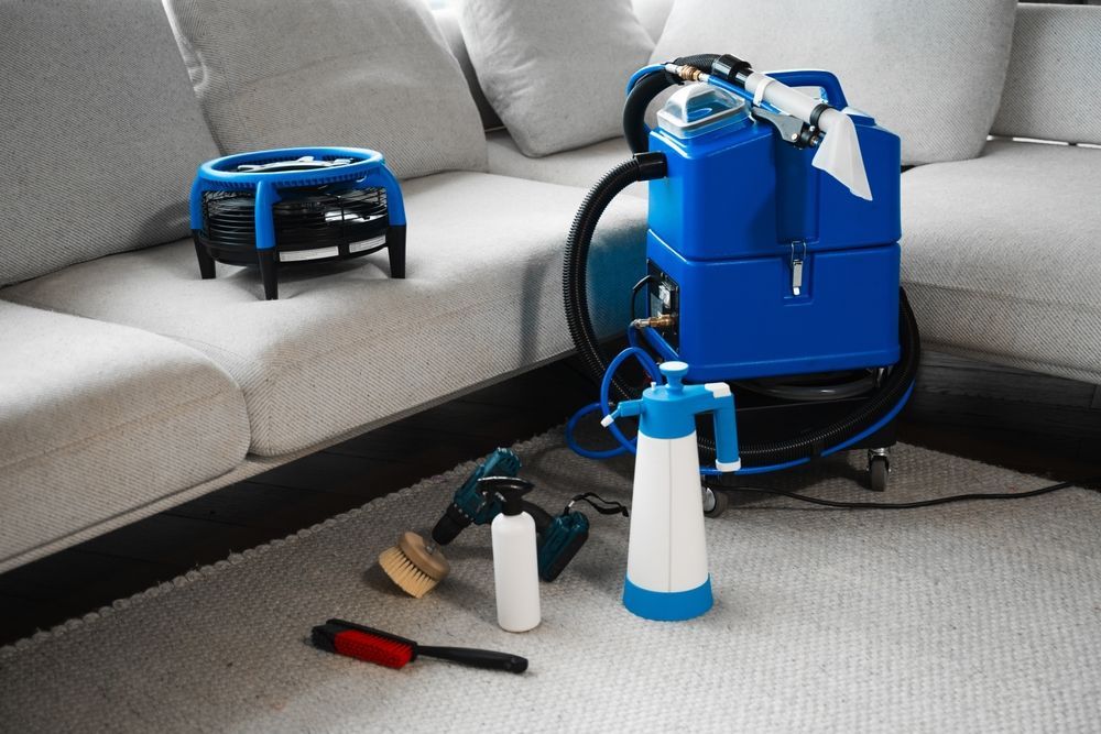 Carpet cleaning equipment on a light-colored carpet next to a white couch with commercial cleaning service