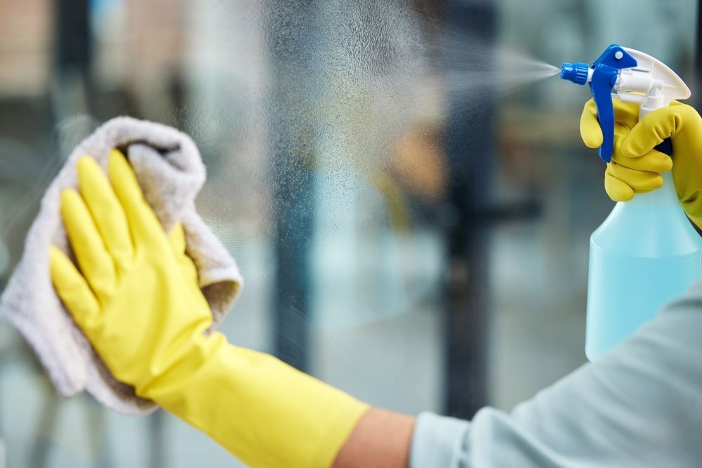 Person in yellow gloves cleaning an office window during standard vs deep office cleaning