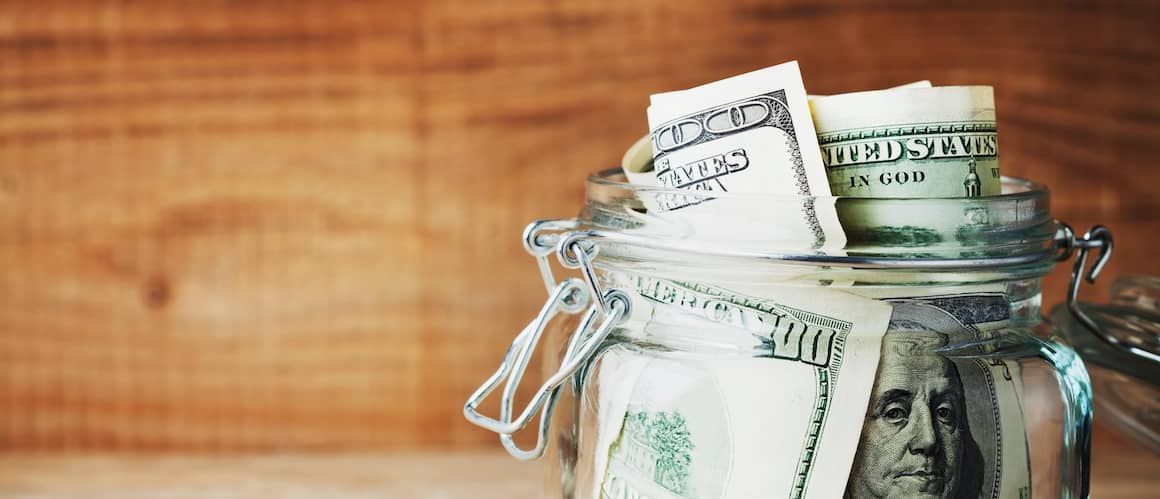 Jar filled with American dollar bills, sitting in front of a wood background.