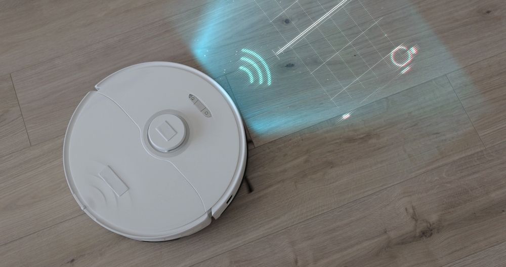 White robotic vacuum on a wooden floor with a blue holographic projection indicating mapping.