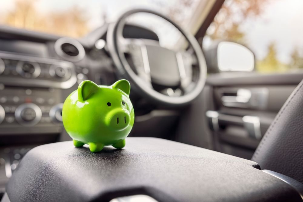 Green piggy bank on a car's center console with the steering wheel and dashboard in the background.