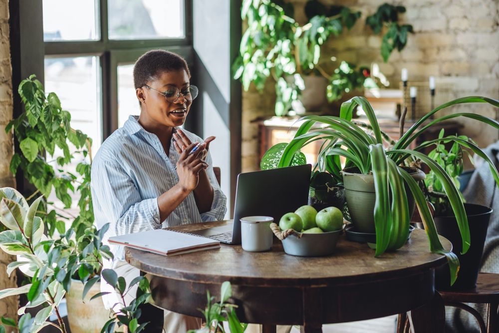 Woman working on a laptop in a sunlit office with plants, representing eco-friendly office cleaning Sydney.