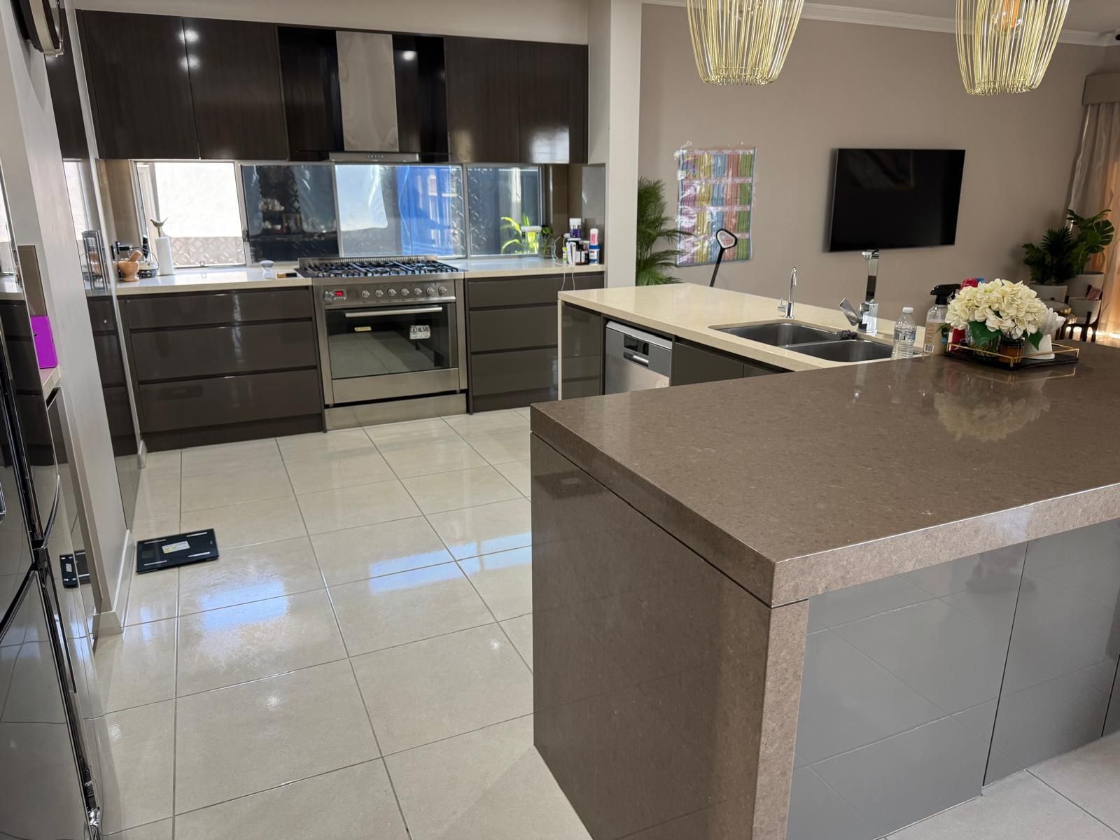 Modern kitchen with brown cabinets, island, and tile floor; stainless steel appliances.