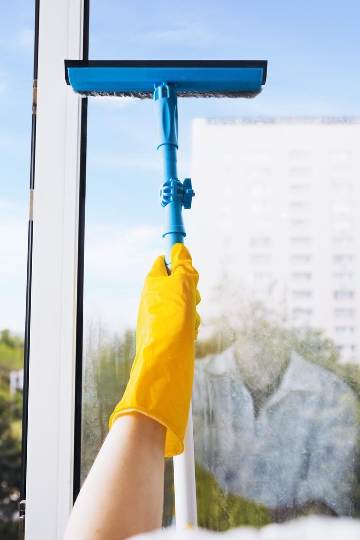Person wearing yellow glove using blue squeegee to clean a window.