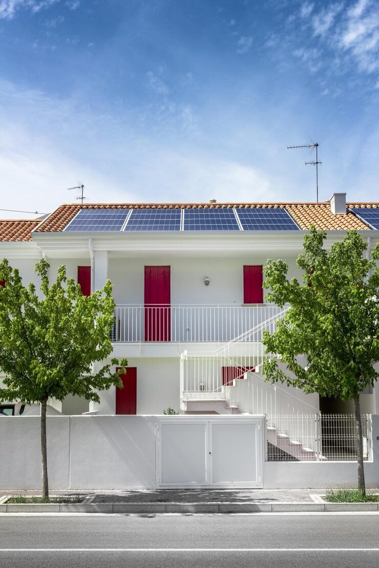 White building with red doors, solar panels on the roof, trees in front, and a blue sky.