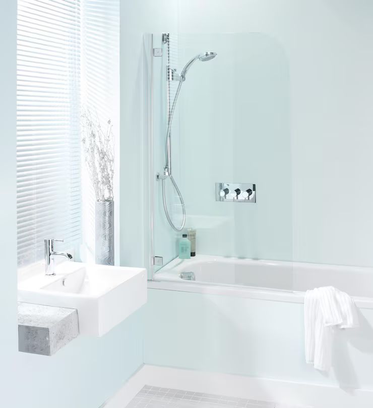 Bathroom with a bathtub, showerhead, glass screen, and a small sink. Light blue walls and white fixtures.
