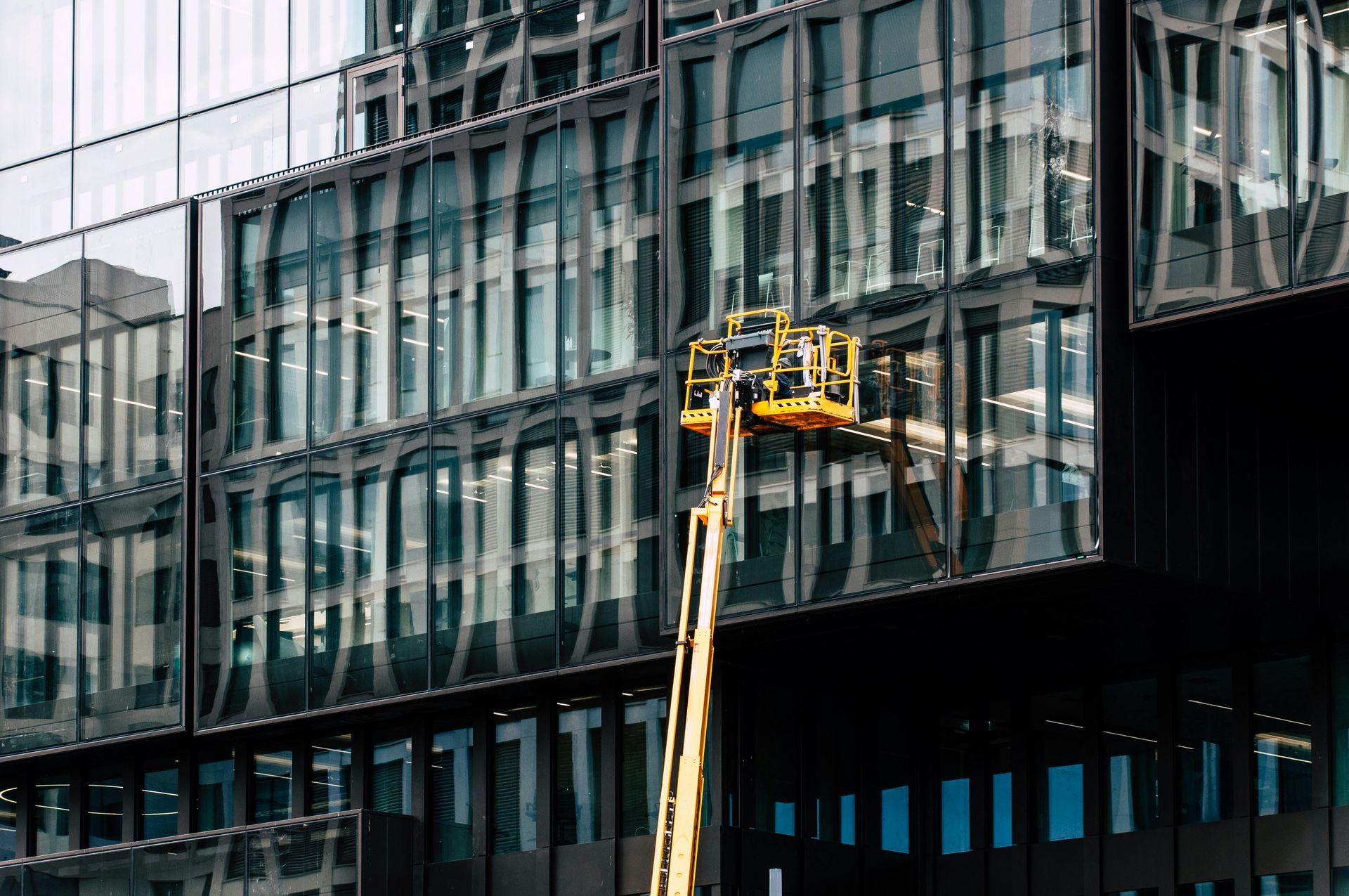 Worker in a yellow lift cleaning a modern glass office building facade