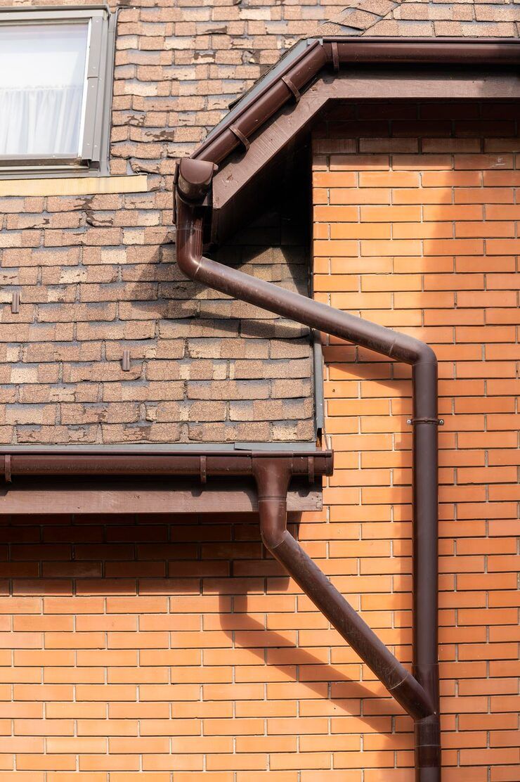 Brown gutters on a brick building with a small window, angled roof.