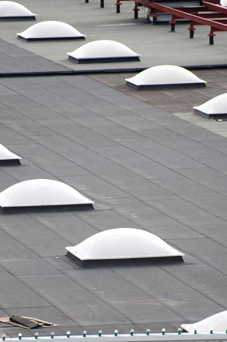 Flat roof with multiple white, dome-shaped skylights and dark roofing material.