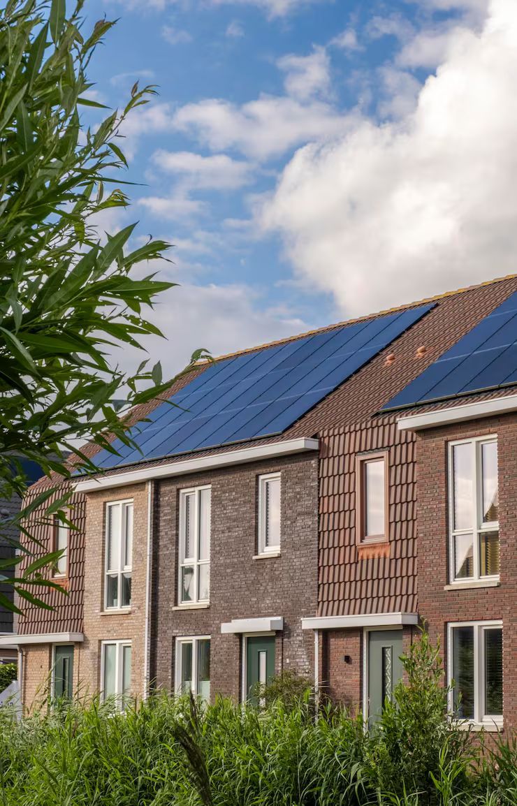 Row of brick houses with solar panels on the roof and tall windows, under a blue cloudy sky.