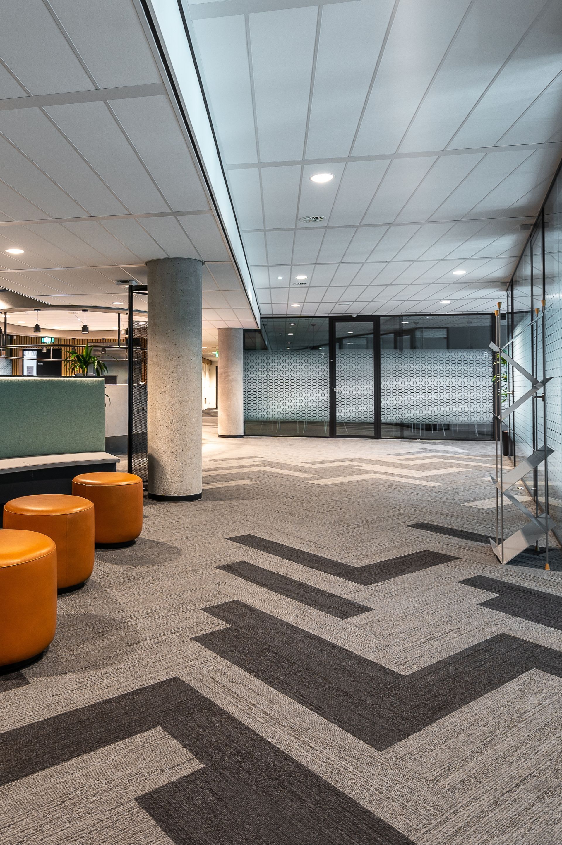 Modern office lobby with patterned carpet, orange ottomans, and decorative frosted glass doors.