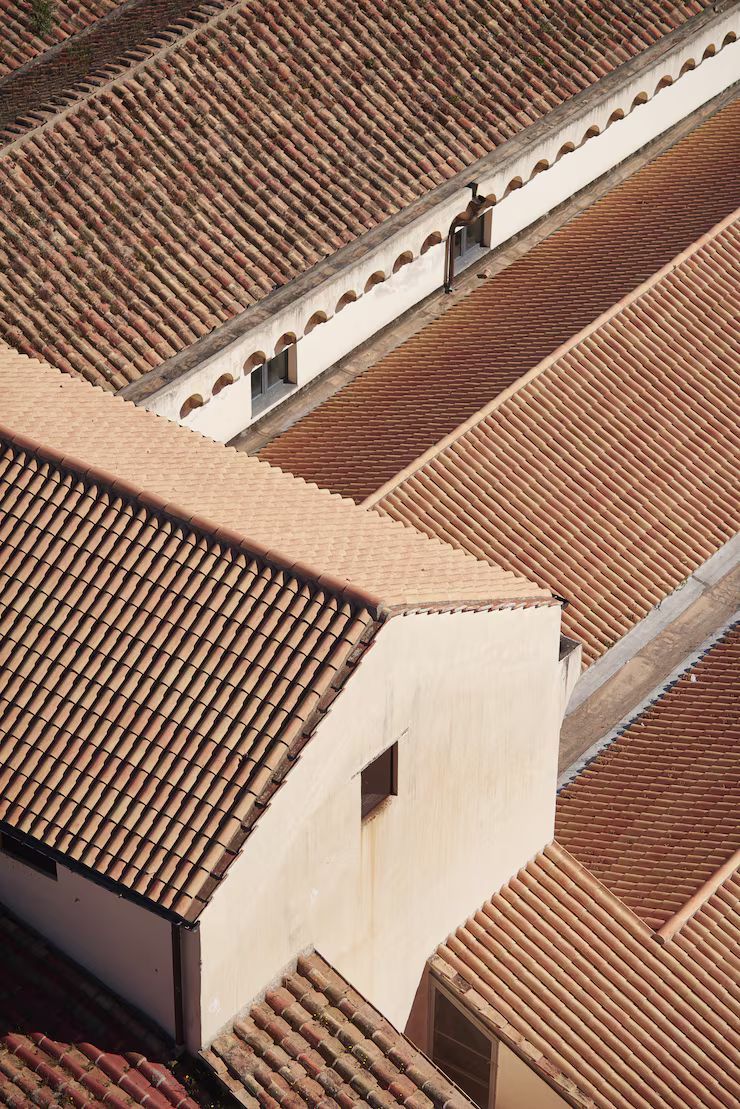 Overhead view of several buildings with terracotta tile roofs, a few with small windows, in bright daylight.