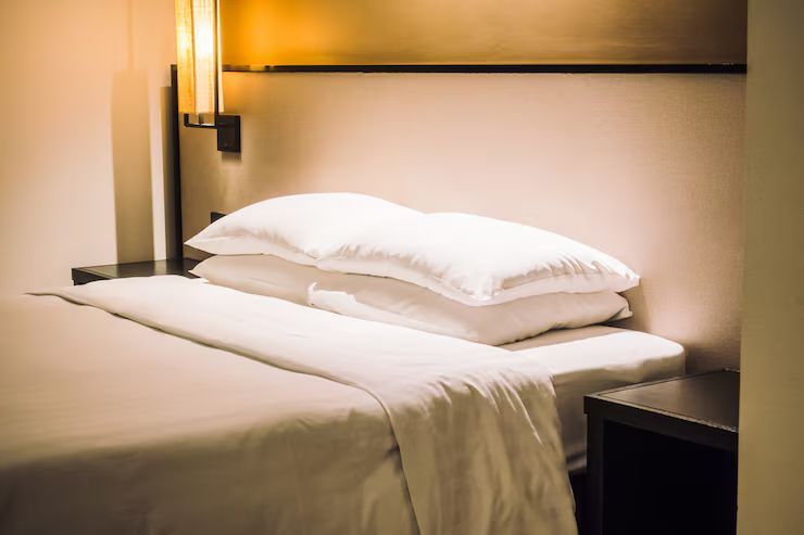 A neatly made bed with white linens and two stacked pillows in a hotel room.
