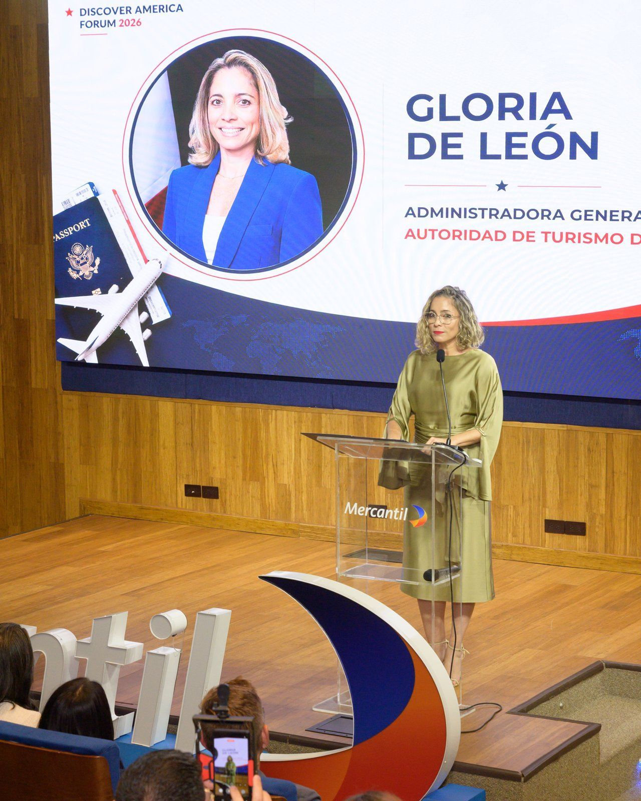 Intervención de Gloria De León; la pantalla del evento muestra su nombre y cargo.