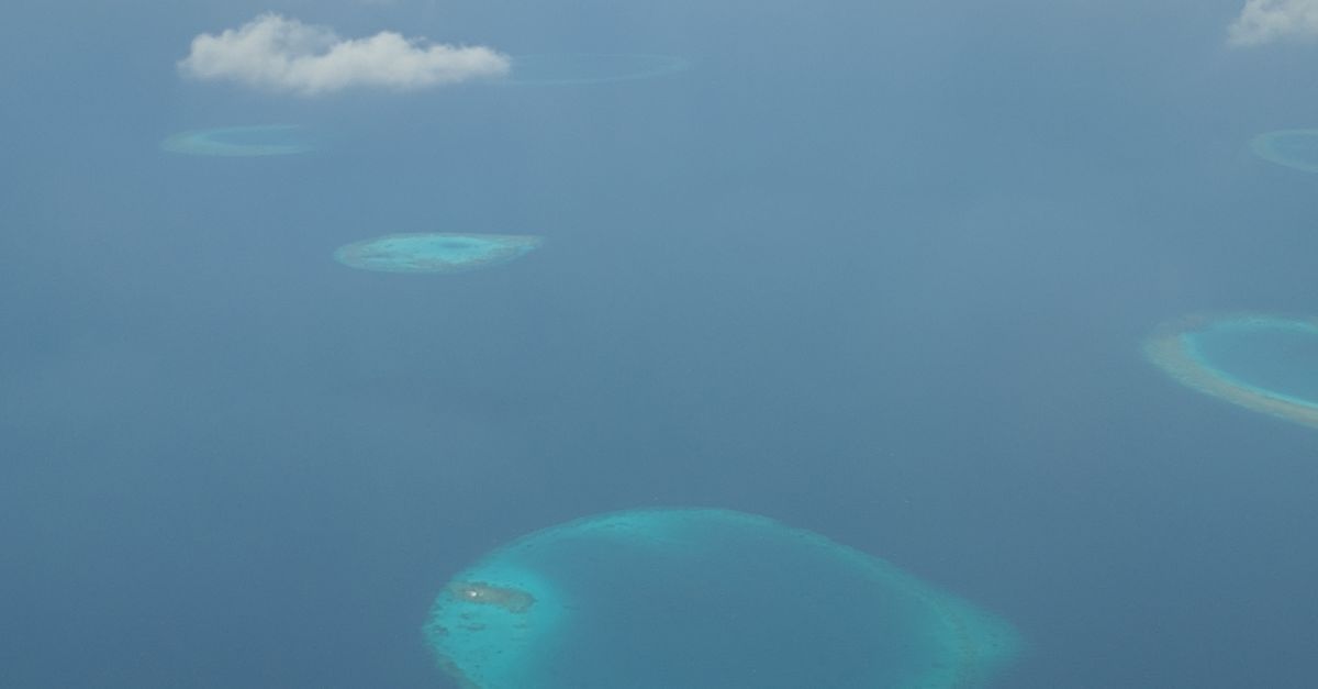 Passenger aircraft flying above turquoise Maldives islands and resort atolls