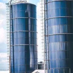 Two tall blue industrial silos with metal ladders against a cloudy sky