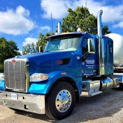 Blue semi-truck parked outdoors on gravel under a partly cloudy sky