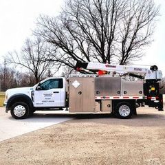 White utility truck with crane and storage compartments parked outdoors near bare trees