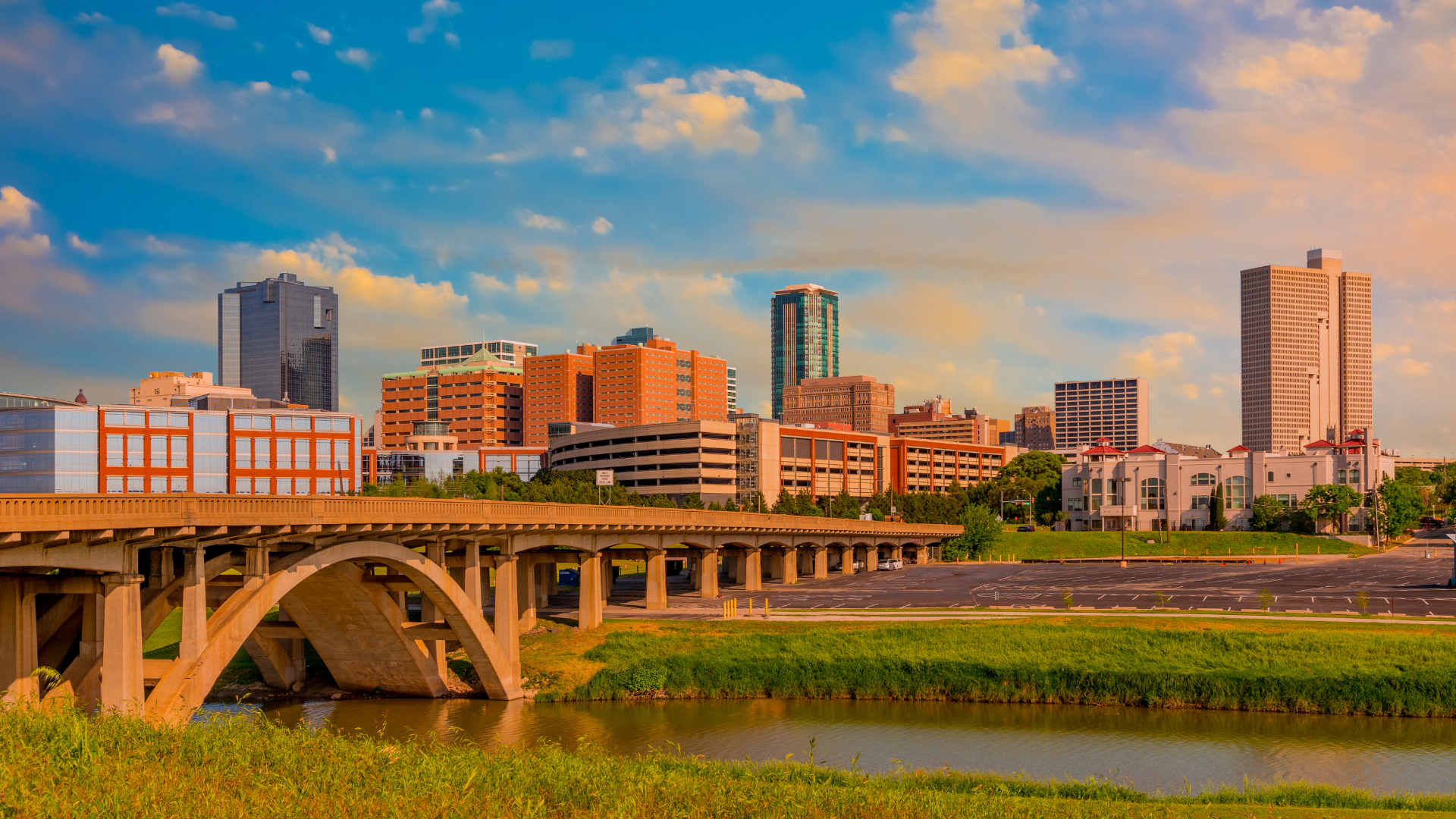City skyline at sunset with a bridge over a river and colorful clouds overhead