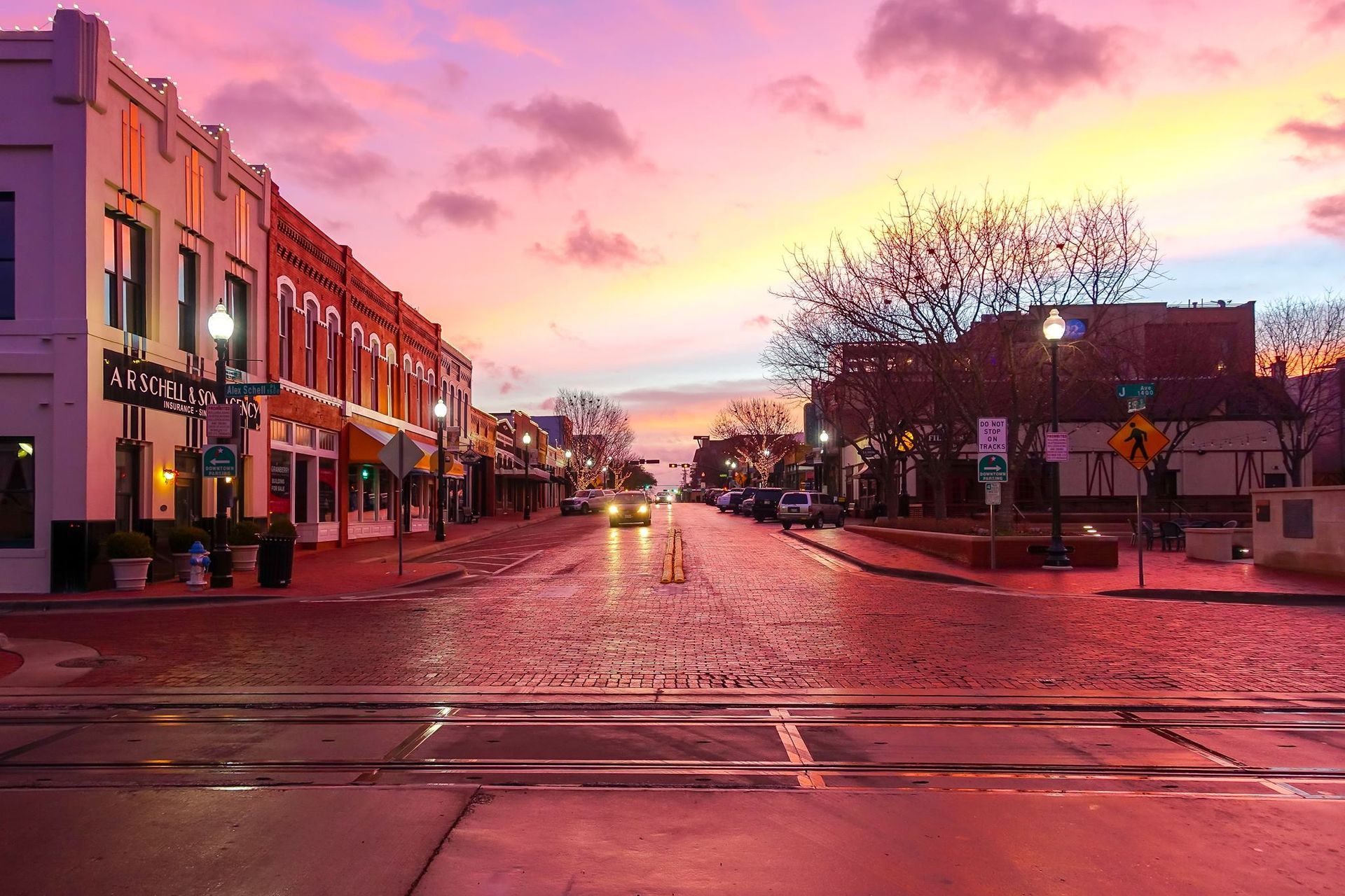 Sunset over a quiet downtown street with pink sky and storefronts reflecting on wet pavement