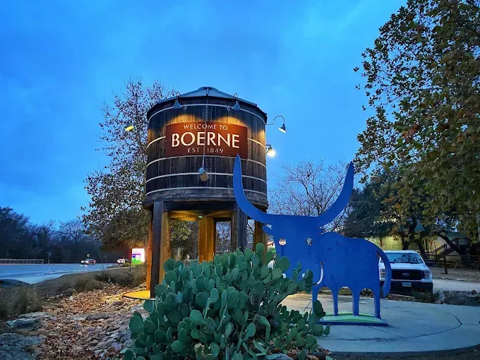 Boerne water tower at dusk with illuminated sign and blue animal sculpture in front