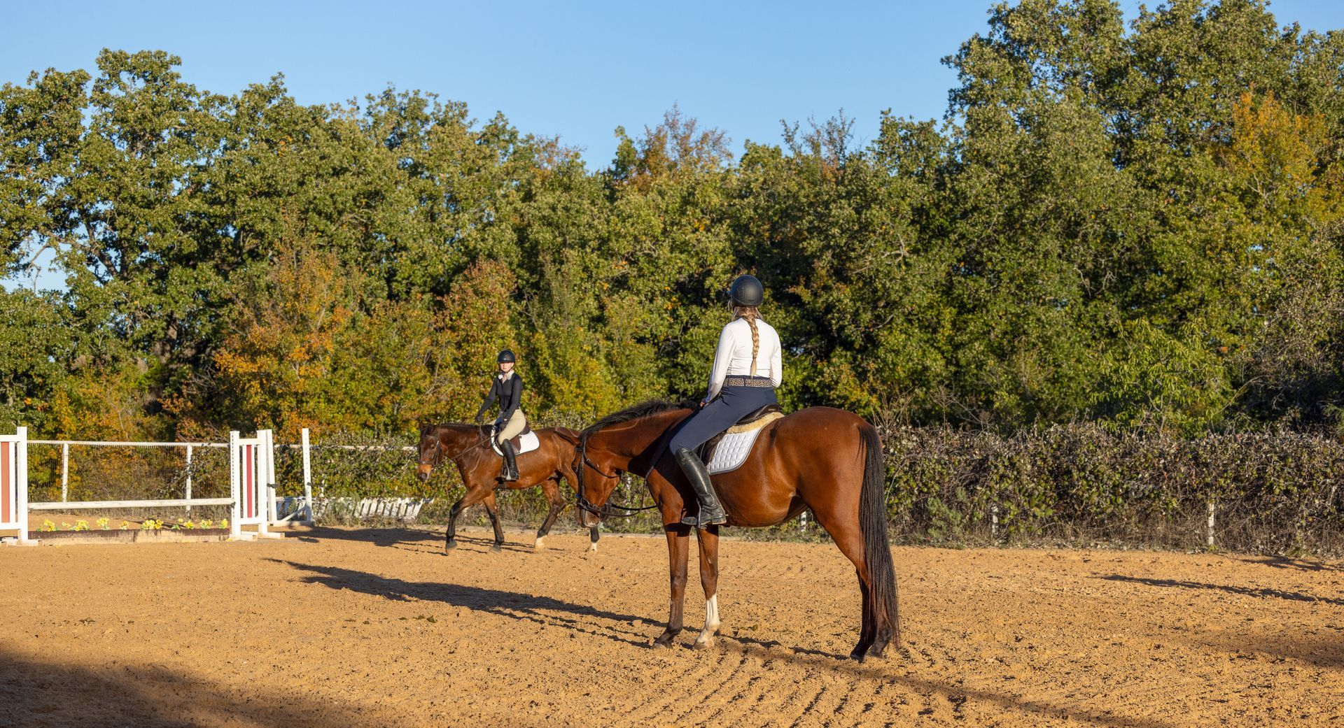 Two people are riding horses in a dirt arena.