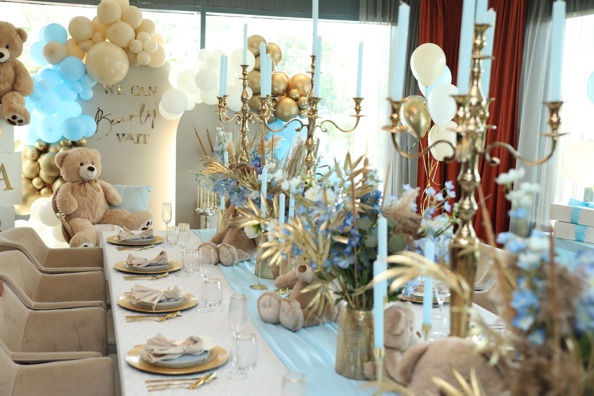 Tafeldecoratie met teddybeer-thema, in blauw, goud en crème, inclusief ballonnen en kaarsen.