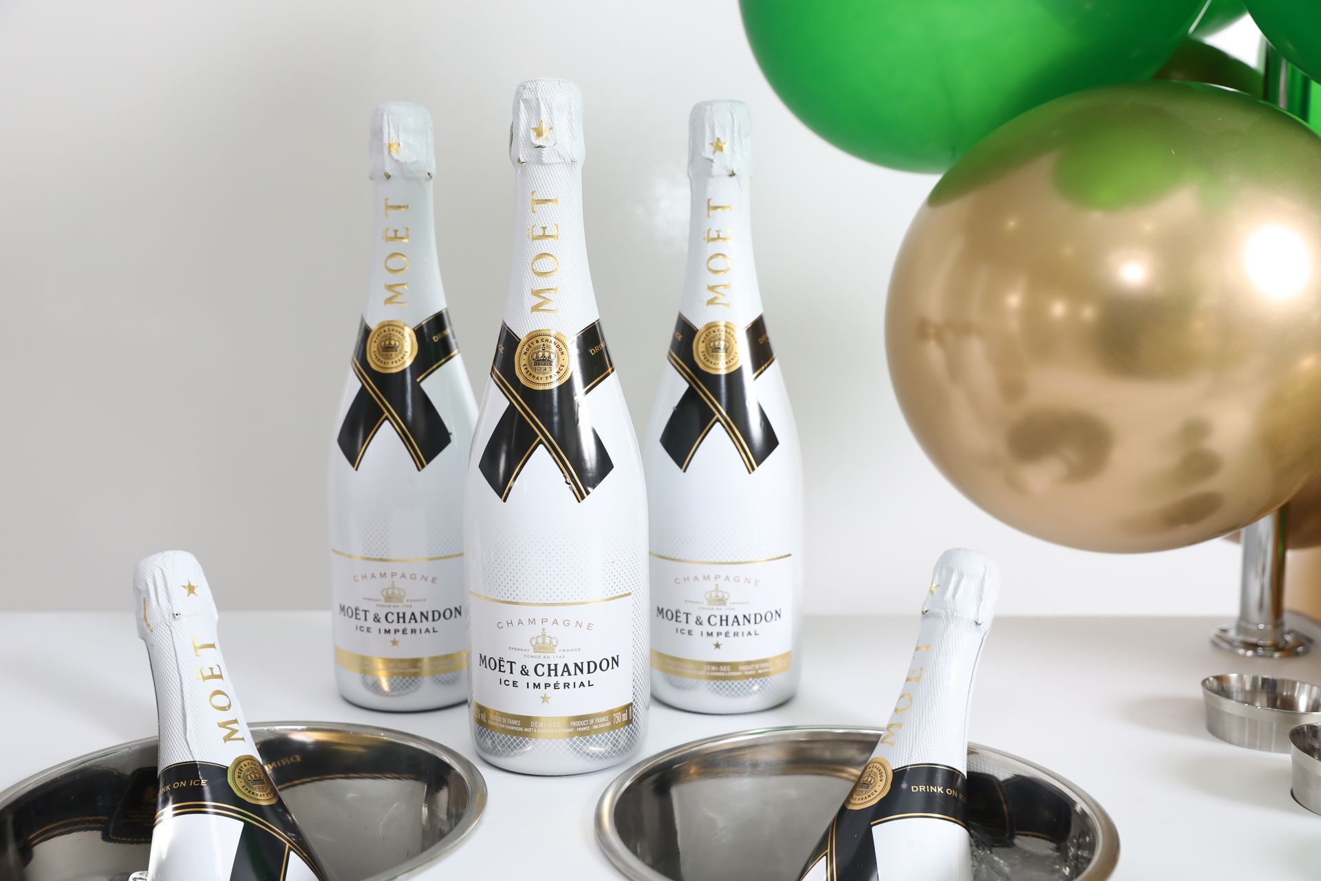 Champagneflessen in ijsemmers, met groene en gouden ballonnen op de achtergrond.