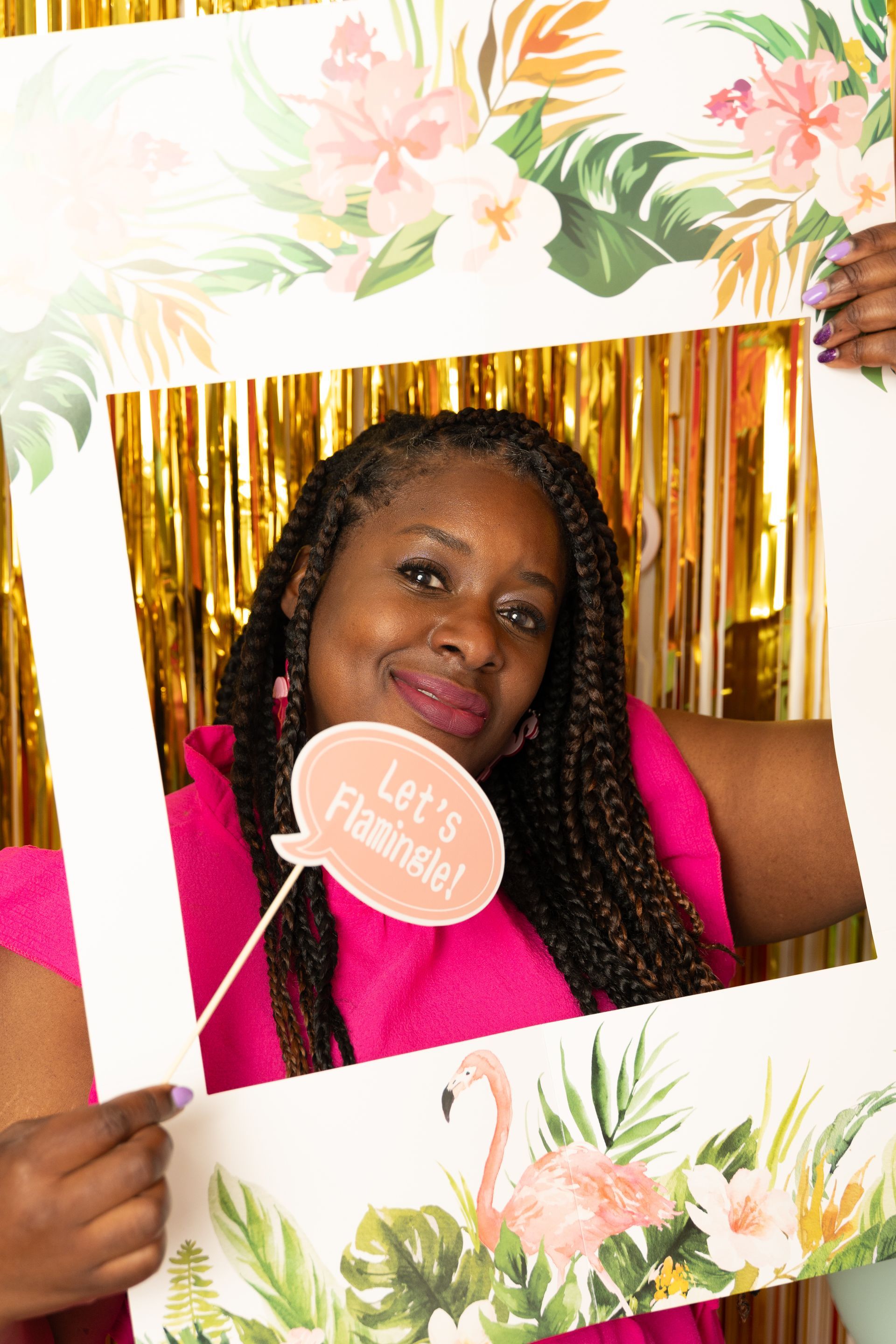 Vrouw in roze jurk, omlijst door een tropisch fotohokje-accessoire. Houdt een bord vast met de tekst 