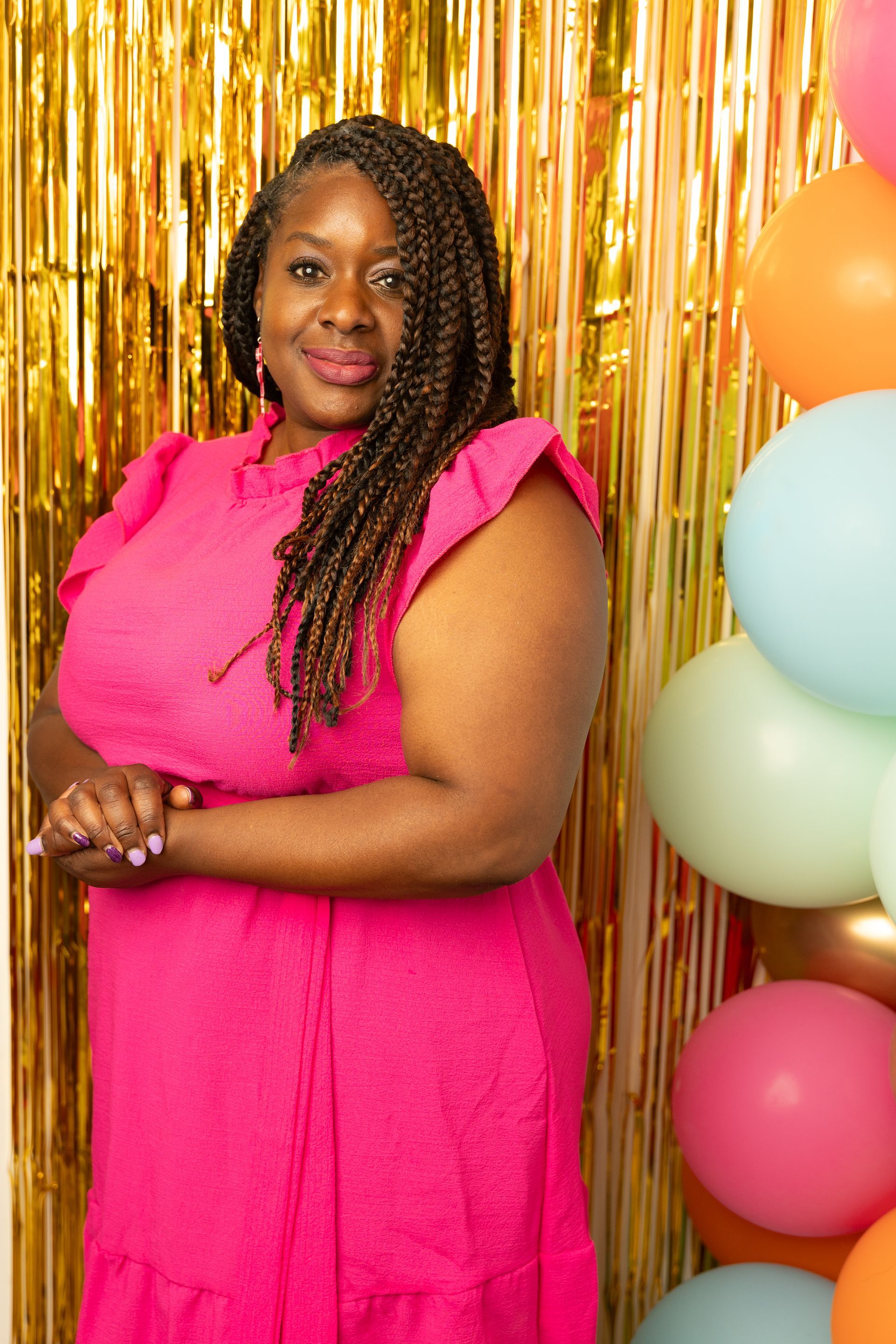 Een vrouw in een roze jurk staat naast ballonnen en gouden franjes.