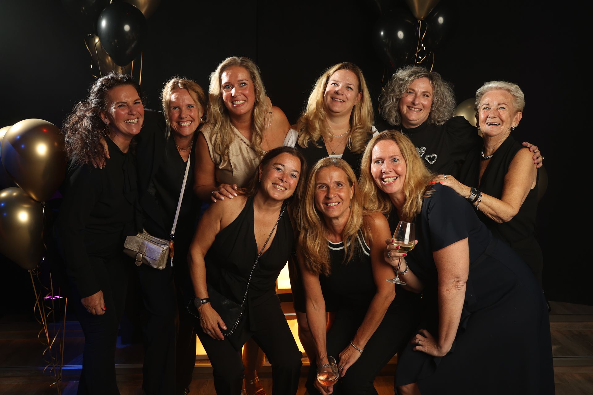 Een groep lachende vrouwen poseert voor een foto. Ballonnen op de achtergrond.