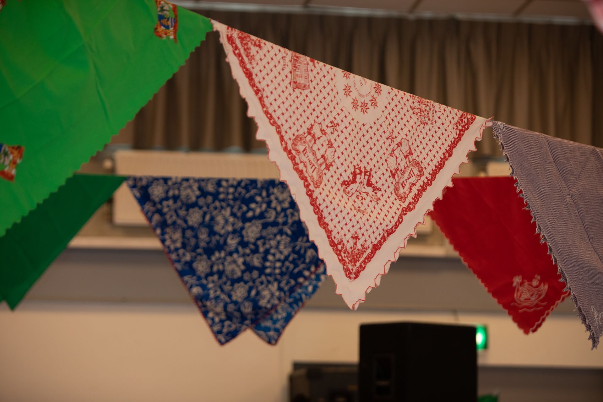 Kleurrijke driehoekige vlaggen, waaronder groene, blauwe, rode en witte vlaggen met patronen, hangen verspreid over de kamer.