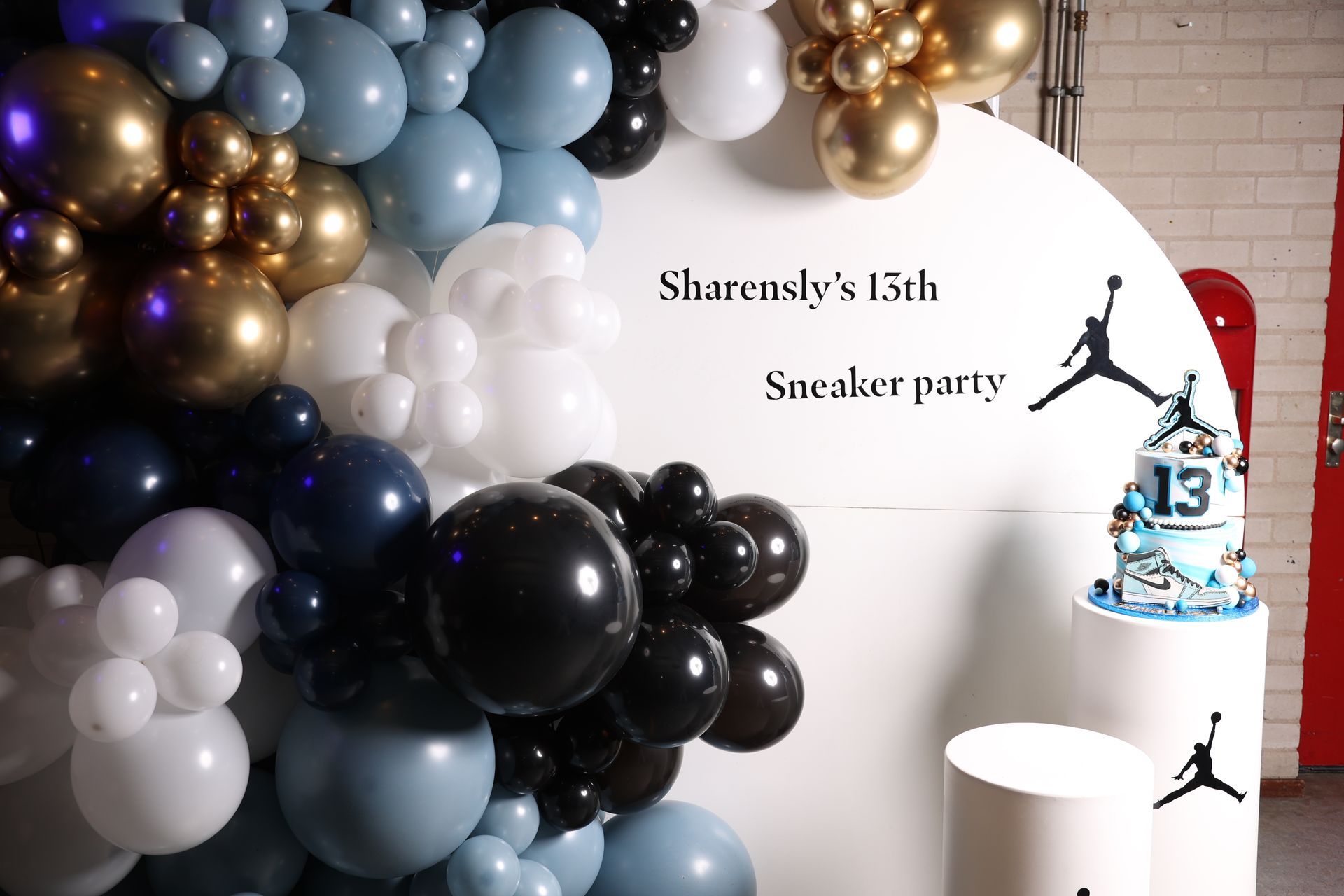Feestdecoratie: ballonnen (goud, blauw, zwart, wit), taart op een standaard met logo en tekst: 