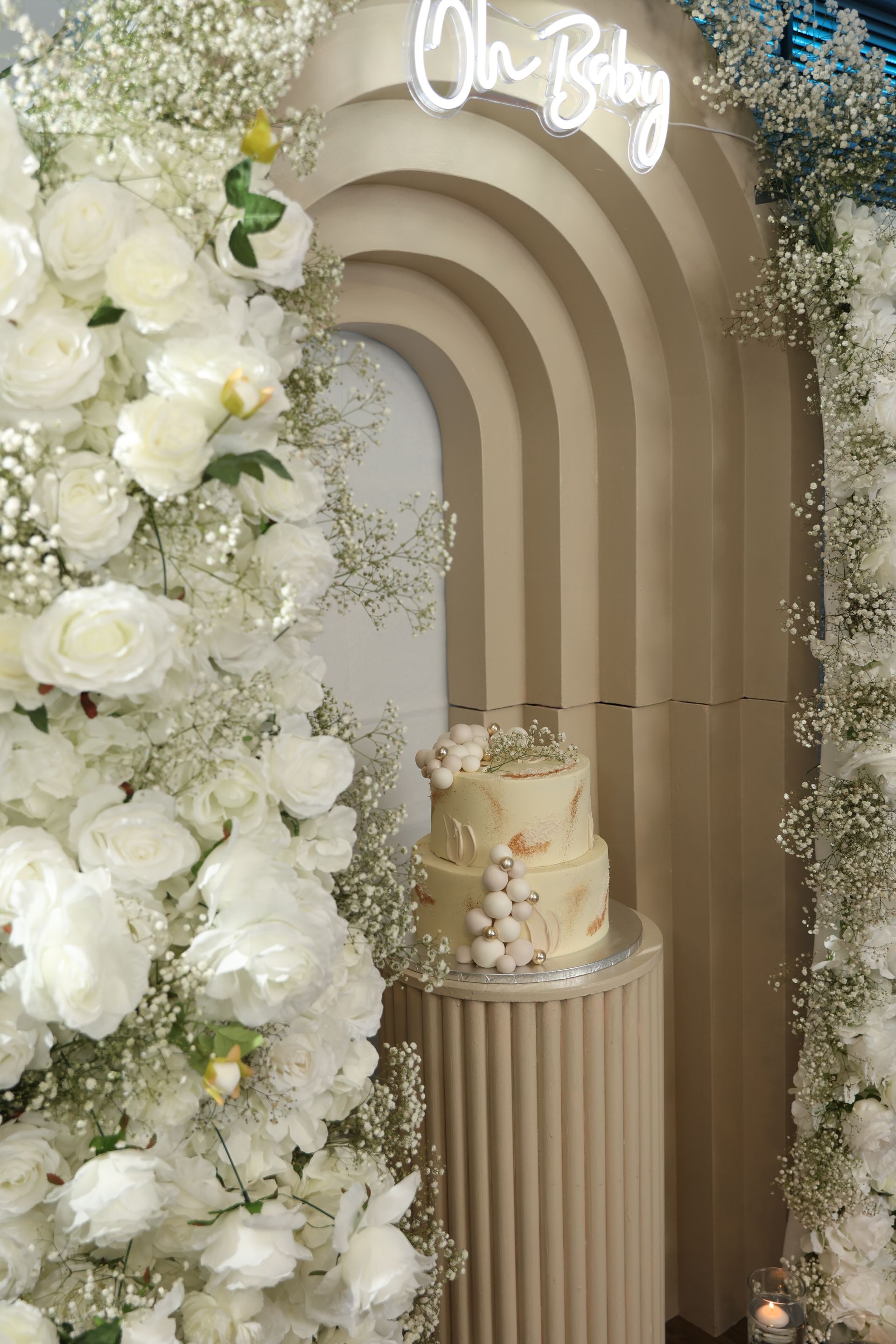 Decoratie voor een babyshower met een taart en bloemstukken; licht kleurenpalet, neonbord met de tekst 
