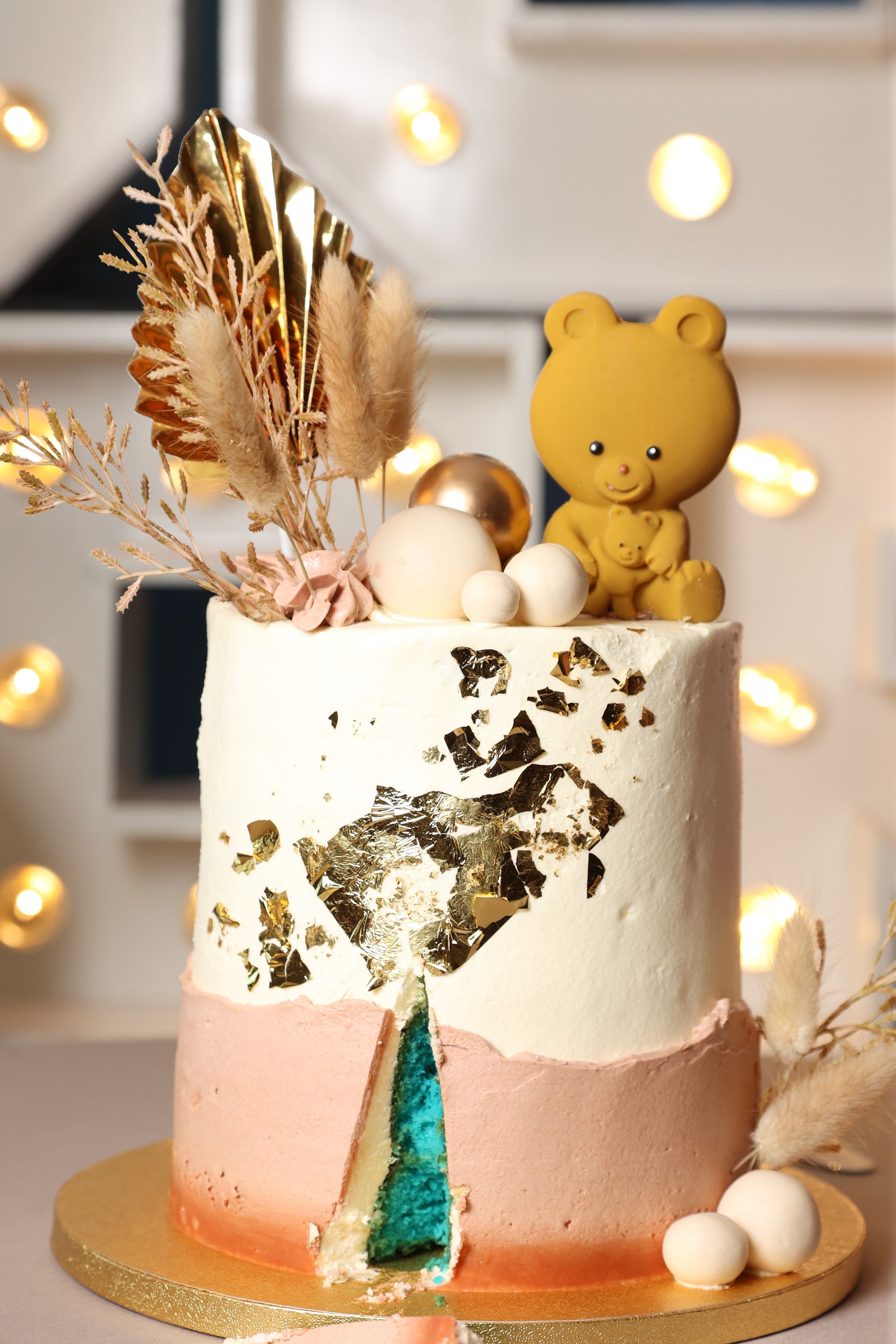 Taart met bladgoud en een teddybeer als decoratie. Roze en witte glazuur.