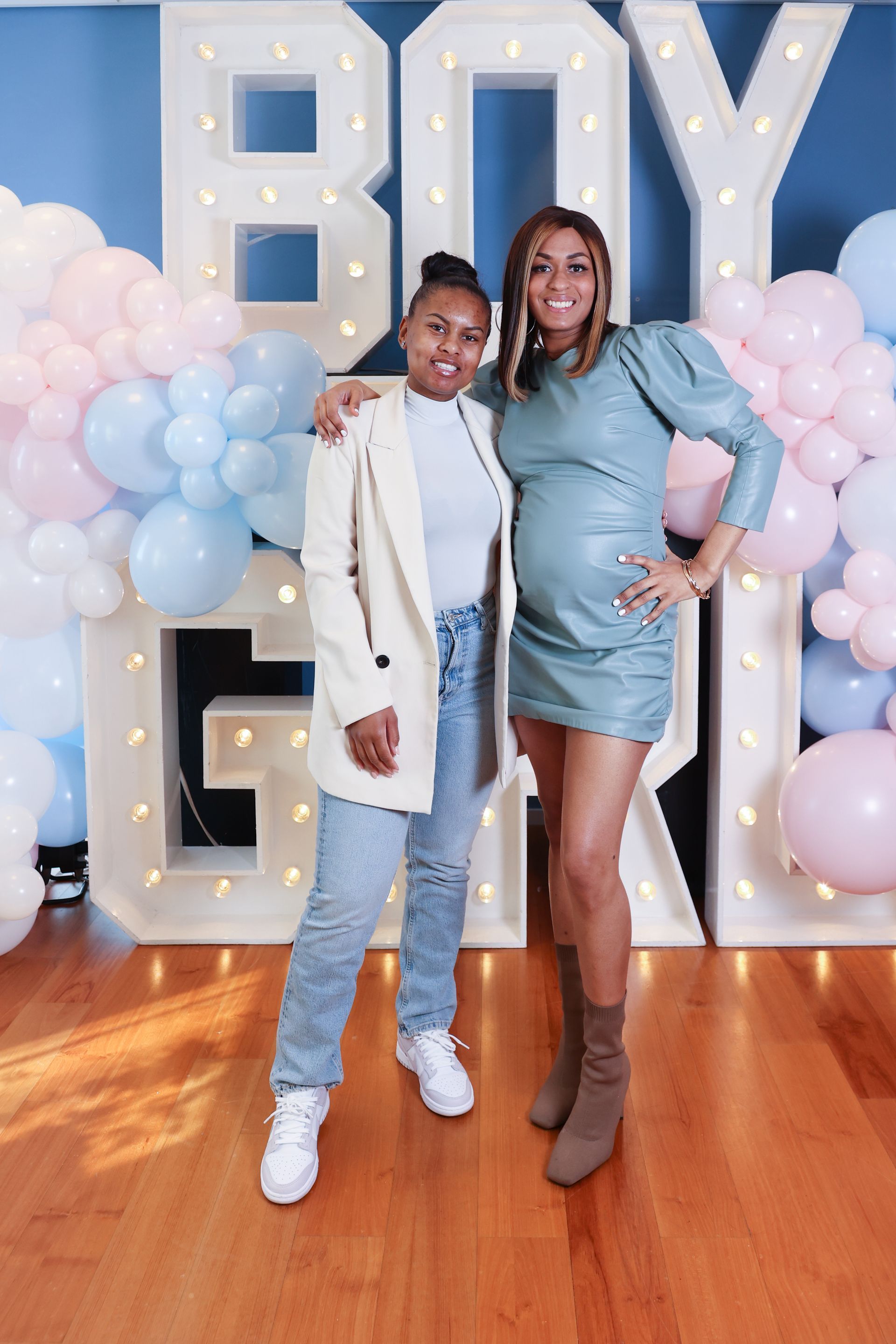 Twee vrouwen poseren voor een foto op een babyshower met een bordje 