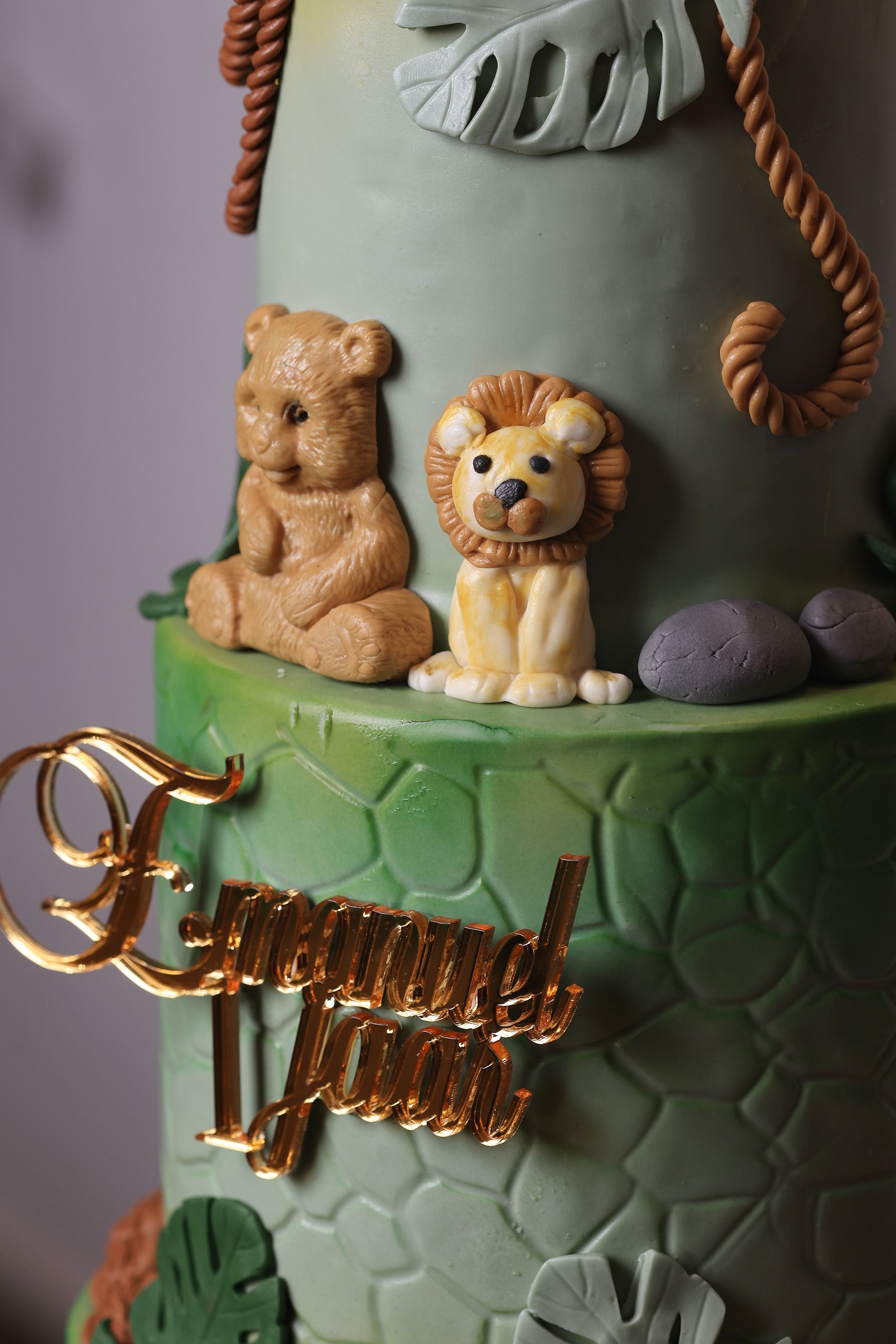 Een taart met junglethema, versierd met een leeuw en een beer van fondant, touwaccenten en een gouden 