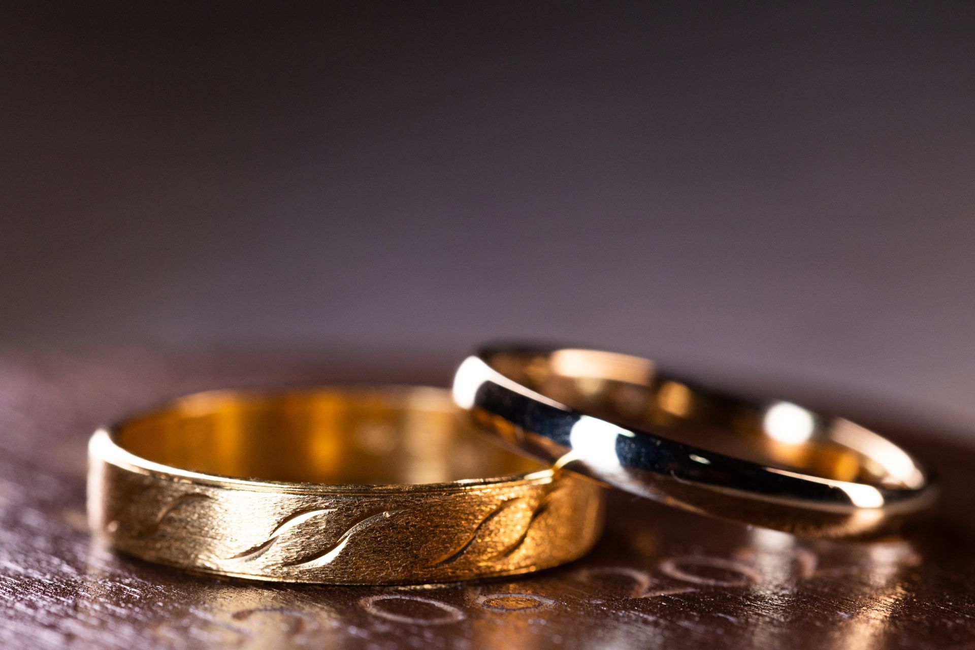 Twee gouden trouwringen, de ene met een golvend patroon, de andere glad, op een reflecterend oppervlak.