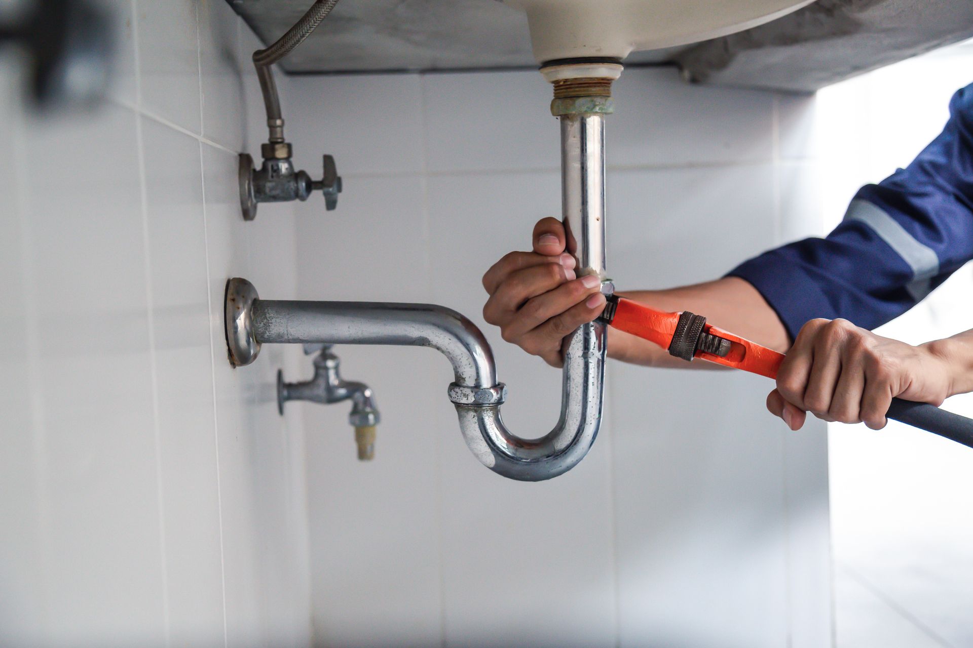 Plumber tightening a sink drain pipe with a wrench under a bathroom basin
