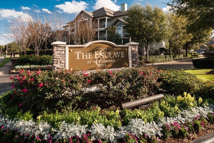 Entrance sign for The Enclave at Woodbridge with landscaped flower beds.