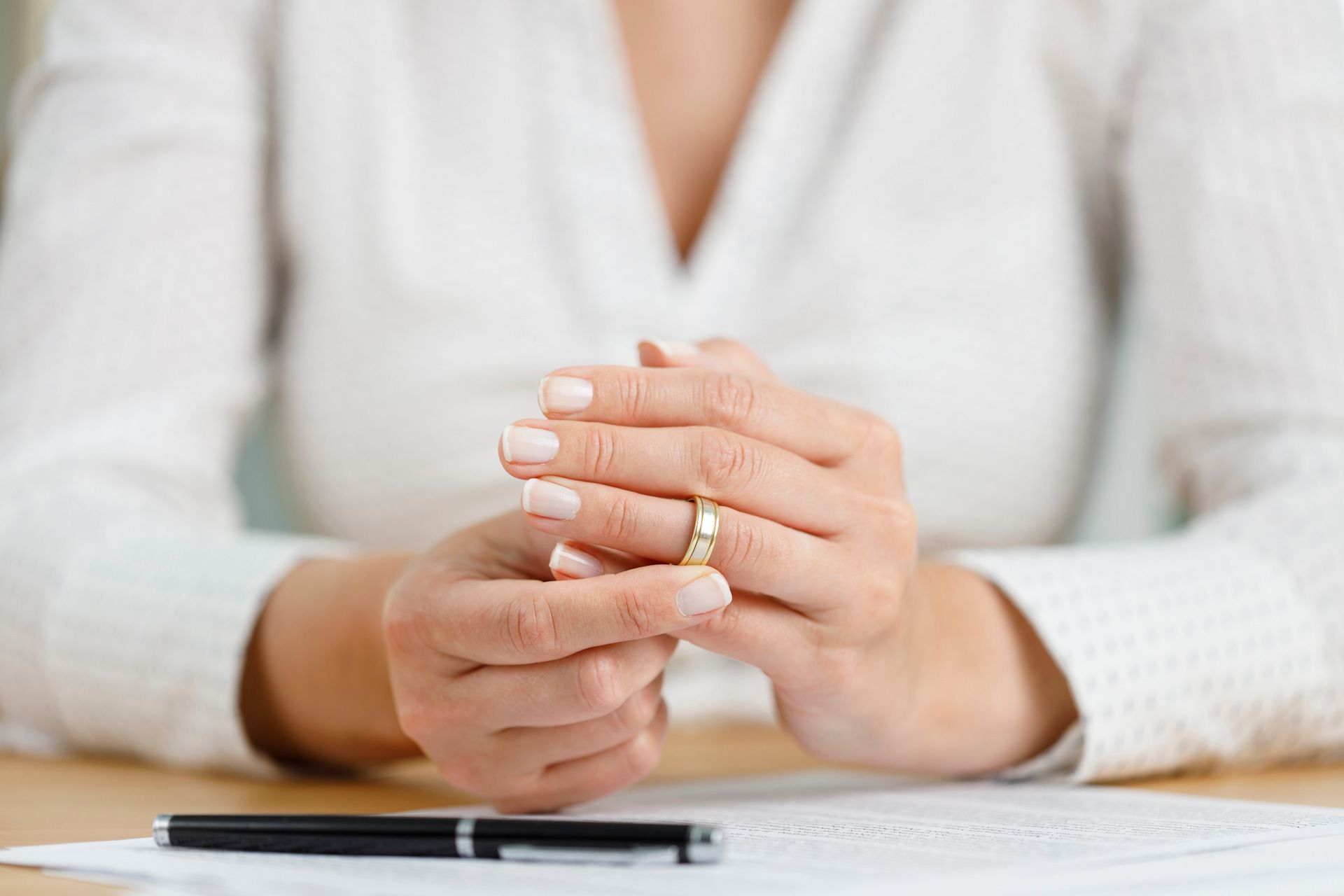 A woman is sitting at a table holding a wedding ring in her hands.